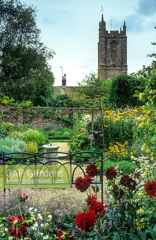 View of formal garden with blue painted wrought iron bench, old sundial, gravel paths, roses, herbaceous perennials - Cerne Abbas, Dorset