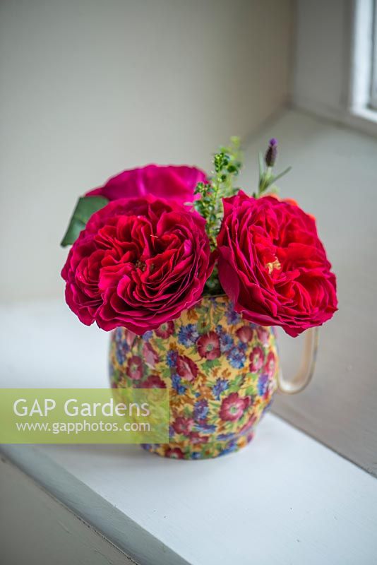 A cut flower arrangement of roses in a patterned jug on a windowsill