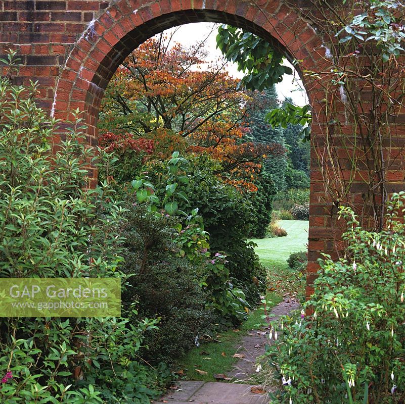 Brick arch frames view of path leading to main lawn, overhung by Parrotia persica, its leaves turning red and gold for autumn.