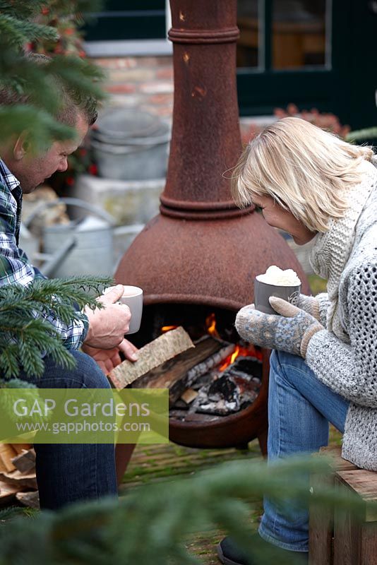 Man and woman enjoying warmth from Chiminea