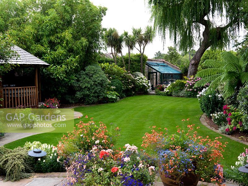 A town garden with a lawn, covered seating area, greenhouse and annual containers.