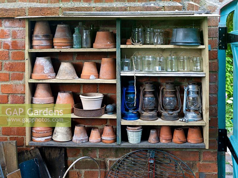 Shelves built from reclaimed timber offcuts house terracotta plant pots, glass jars and lanterns, making use of a wall for storage in this tiny town garden.