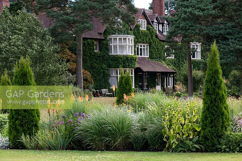 A view of Abbeywood House, an Edwardian residence built in 1908, seen  accross a herbaceous border of perennials, grasses and repeated coonifers.