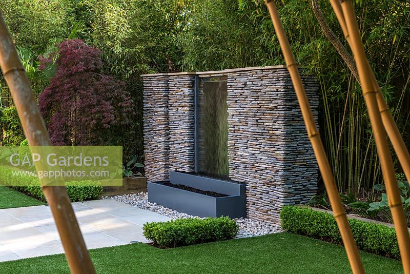 Town garden designed by Kate Gould. Stainless steel water feature set into a dry stone wall. Boundary beds are filled with bamboo,  acer, Trachycarpus fortunei, hosta and euphorbia.