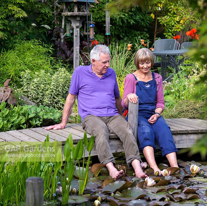 Michael and Jill Hill in their garden Barnwood, a town garden with natural pond, bog area and well established mixed borders.