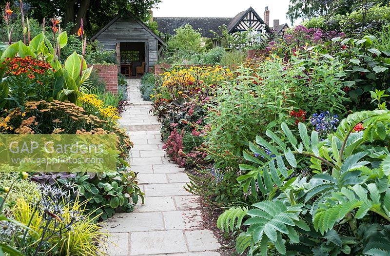 Path through the Lanhydrock Garden, otherwise known as the hot garden, with plants including Melianthus major, Carex elata 'Aurea', salvias, achilleas and tall cannas. Wollerton Old Hall, nr Market Drayton, Shropshire, UK