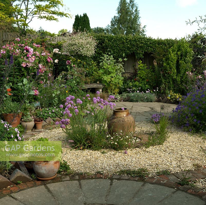 A circular themed gravel garden and patio with cottage garden style planting. Armeria Joystick and a terracotta urn provide a focal point in the centre of the gravel bed