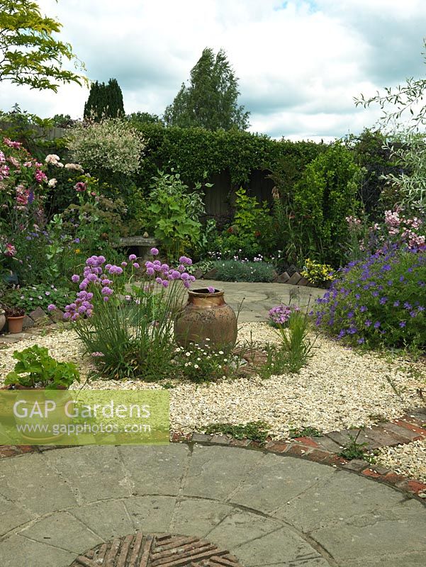 A circular themed gravel garden and patio with cottage garden style planting. Armeria Joystick and a terracotta urn provide a focal point in the centre of the gravel bed.