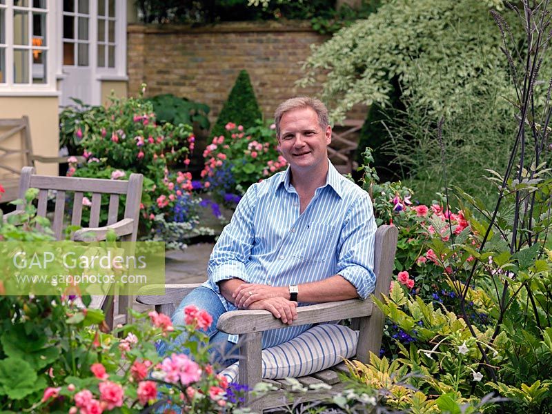 Paul Morrow sits on the terrace amidst pots of busy lizzie, geranium, fuchsia, lobelia, hosta and box.