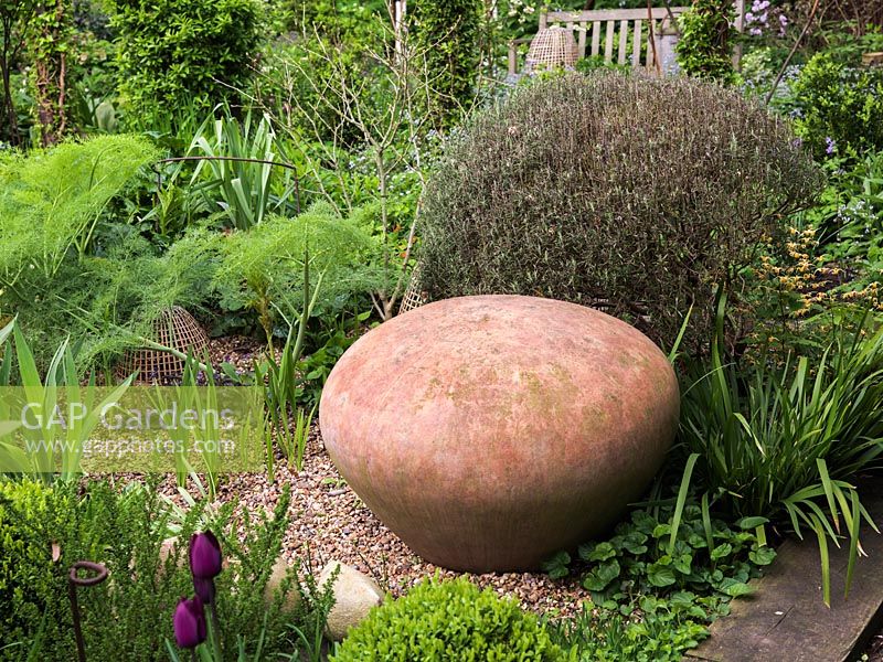 Dome shaped terracotta seat next to rosemary bush in gravel garden with epimedium, fennel and tulips.