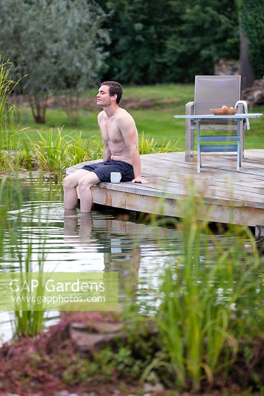 Man relaxing by swimming pond.