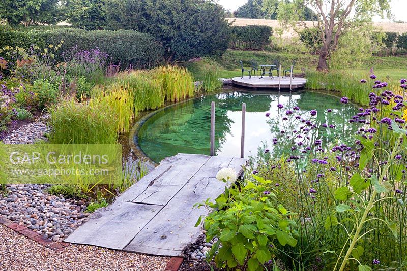 View of wooden decking leading to a swimming pond. 