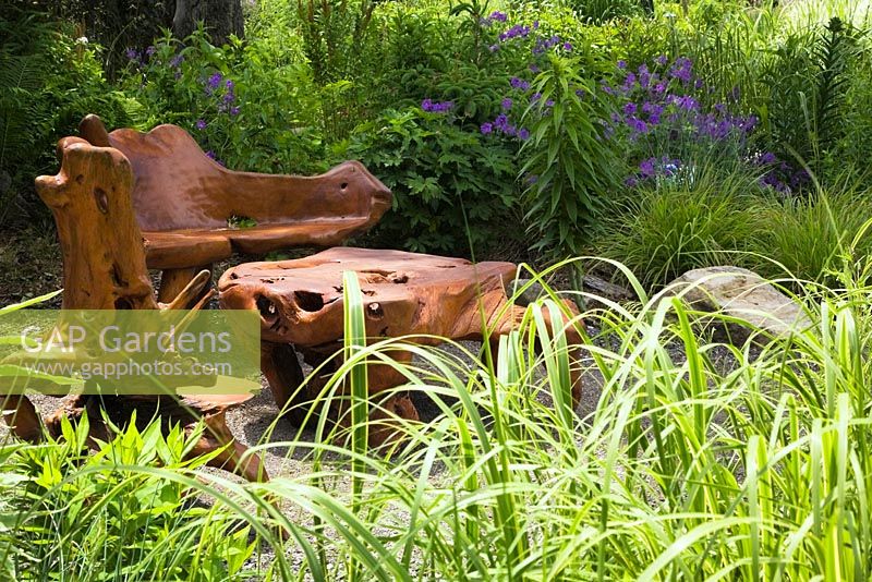 Rustic teak wood chairs and table in the Ornamental Grasses garden in late spring at the Route des Gerbes d'Angelica garden, Mirabel, Quebec, Laurentians, Canada