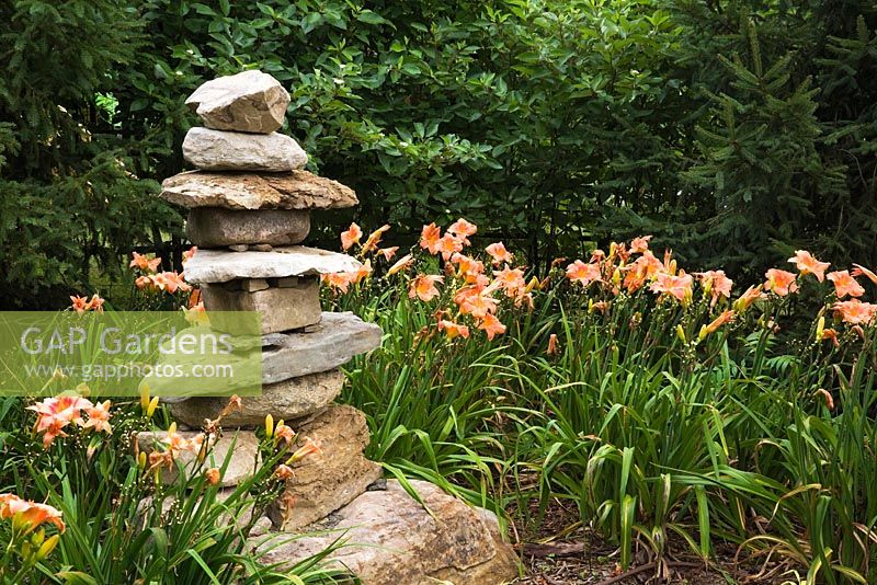 Stacked rock sculpture and orange Hemerocallis 'Strawberry Candy' in the Route des Gerbes d'Angelica garden, Mirabel, Quebec, Laurentians, Canada