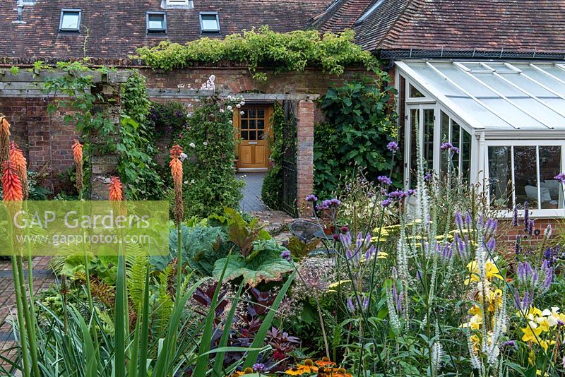 Behind an 1850s coach house conversion, a village garden with mixed beds planted with late flowering  perennials.