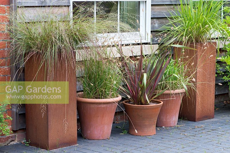 Terracotta and rusted steel containers planted with Phormium tenax, Deschampsia flexuosa and pennisetum ornamental  grasses.