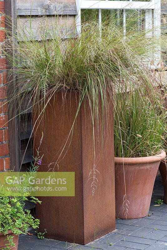 A tall rusted steel container overflows with ornamental grass Deschampsia flexuosa.
