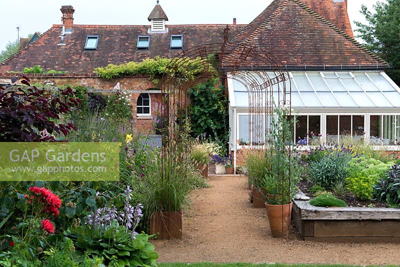 A converted coach house with conservatory and wooden raised beds planted with perennials and herbs.