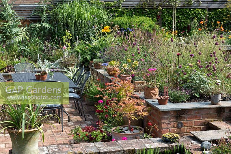 A split level country garden with patio dining area, raised beds with mixed perennials and container planting.