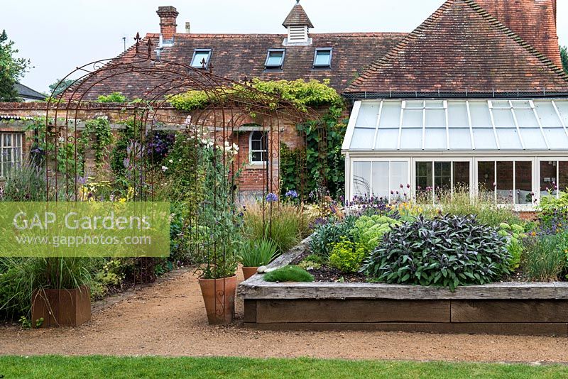 Wooden raised beds planted with perennials and herbs in village garden of old Coach House.