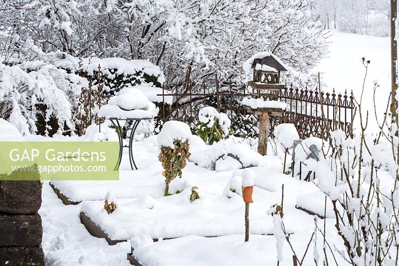 Winter scene in kitchen garden with edged patches, wooden bird feeder, bistro table and a cast iron garden fence