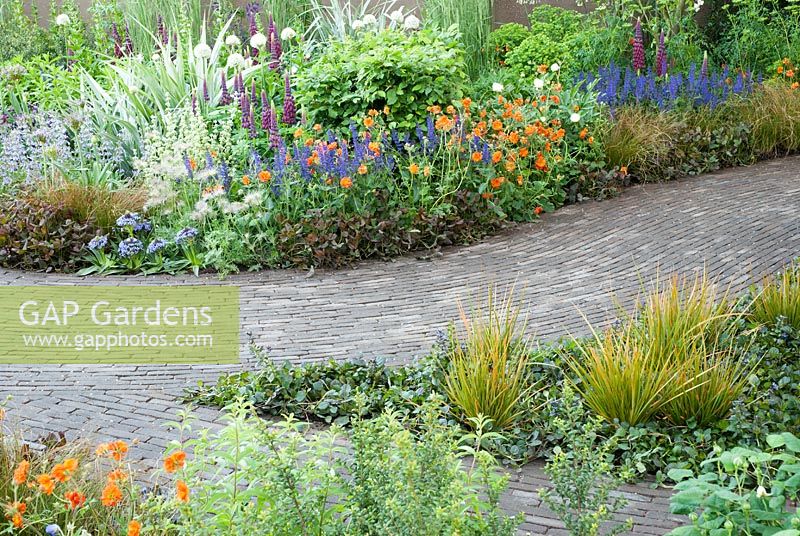 Curved brick path lined with Geum 'Fire Opal', Pulsatilla vulgaris, Scilla peruviana and Lupinus 'Masterpiece' in The Bupa Garden, Design - Cleve West, Sponsor - Bupa, Chelsea Flower Show 2008 - Gold Medal Winners