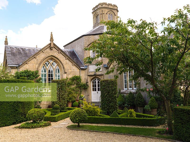 An unusually shaped parterre, using box hedges, yew and imposing cylindrical shapes clipped from Portuguese laurel, flanks the entrance to a former Victorian schoolhouse.