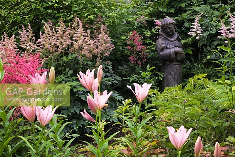 Lilium and Astilbe flowers with statue of a religious monk in border 