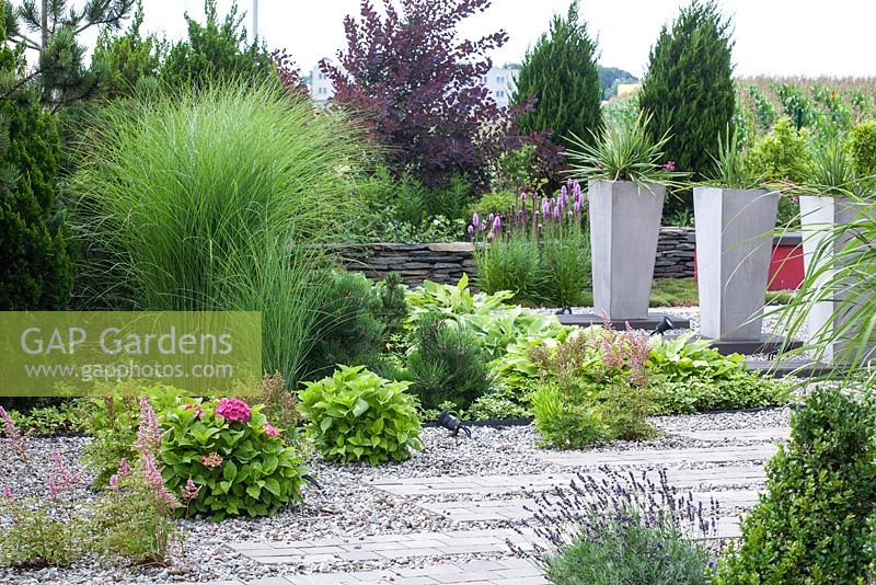 Modern garden with gravel and brick path. Tall containers planted with Yucca filomentosa
