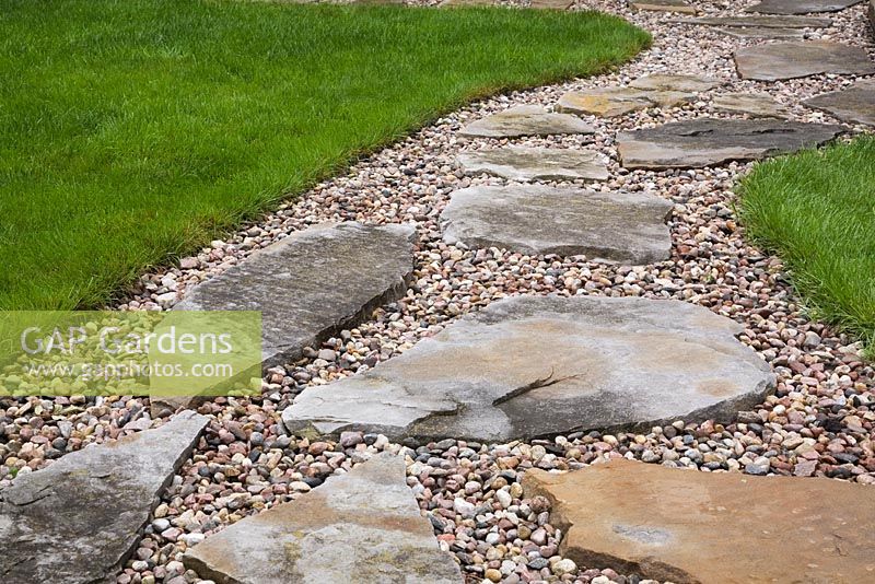 Close-up of flagstone and gravel path through manicured green grass lawn in residential backyard garden in summer