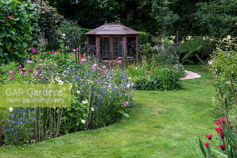 A grass path alongside a colourful wildflower border grown from a packet of annual seed mix. Plants include Poppies, Cosmos, Cornflowers and Viper's Bugloss. A wooden summerhouse behind.