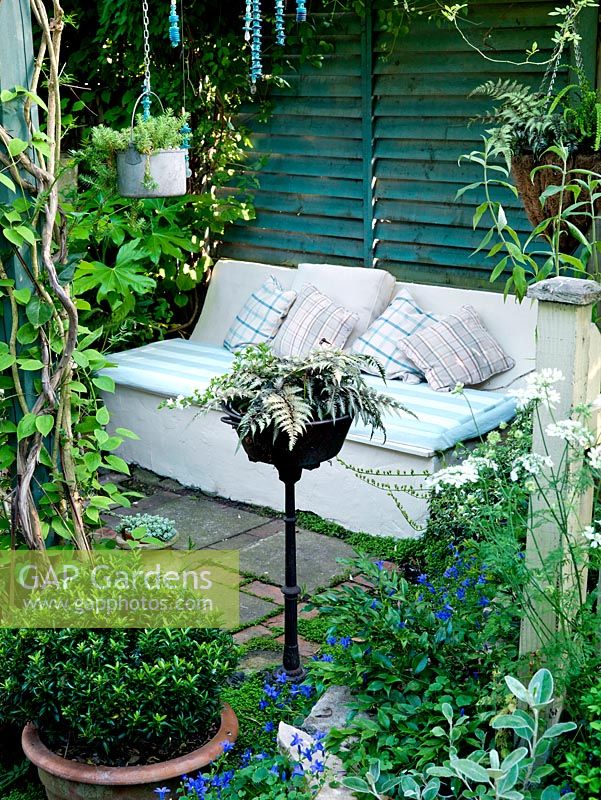 A concrete sofa in shade of pergola and tucked away beside Fatsia japonica. Economic use of space in a tiny garden.