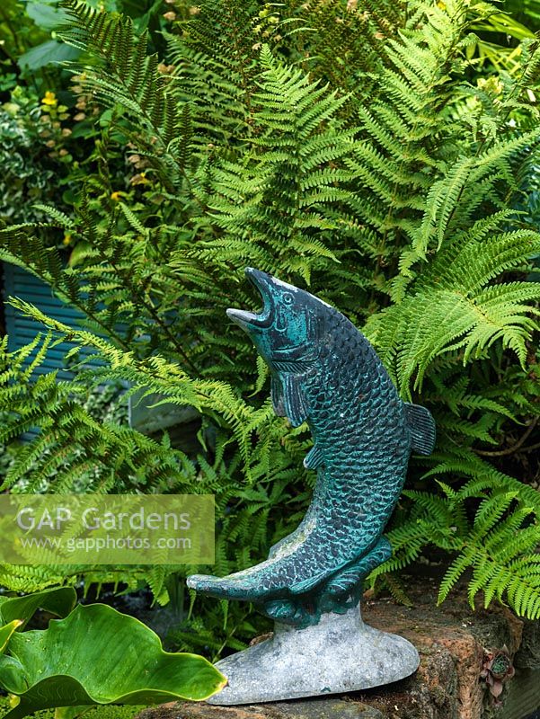 Metal sculpture of a fish tucked away amongst ferns.