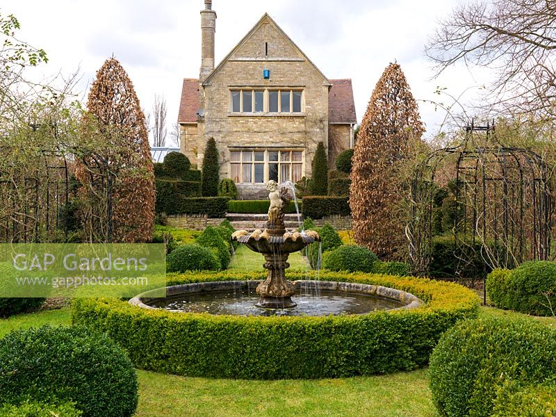 Victorian house overlooks formal French garden with circular pool and fountain, hornbeams, yew topiary and parterres of gold and dark box hedges.