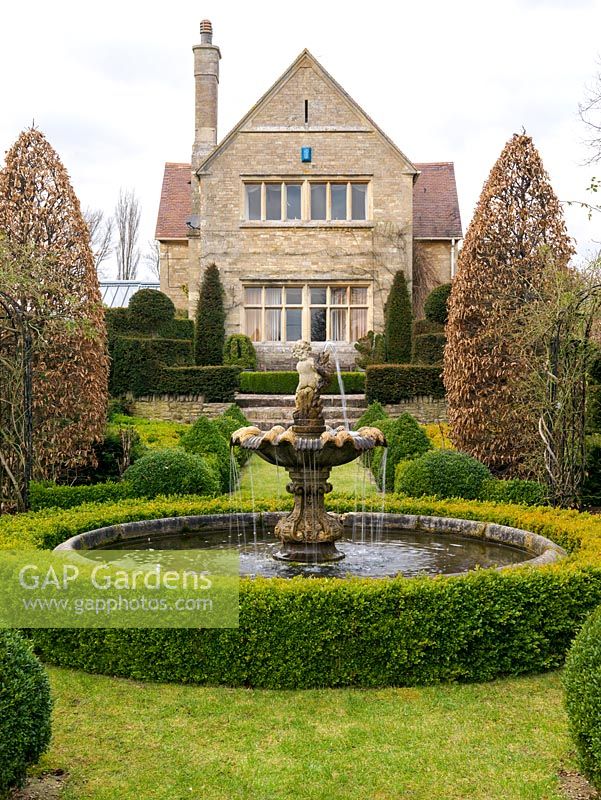 Victorian house overlooks formal French garden with circular pool and fountain, hornbeams, yew topiary and parterres of gold and dark box hedges.