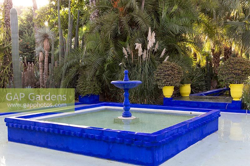Blue fountain and pool with palm trees and cacti at Jardin Majorelle, Yves Saint Laurent garden 