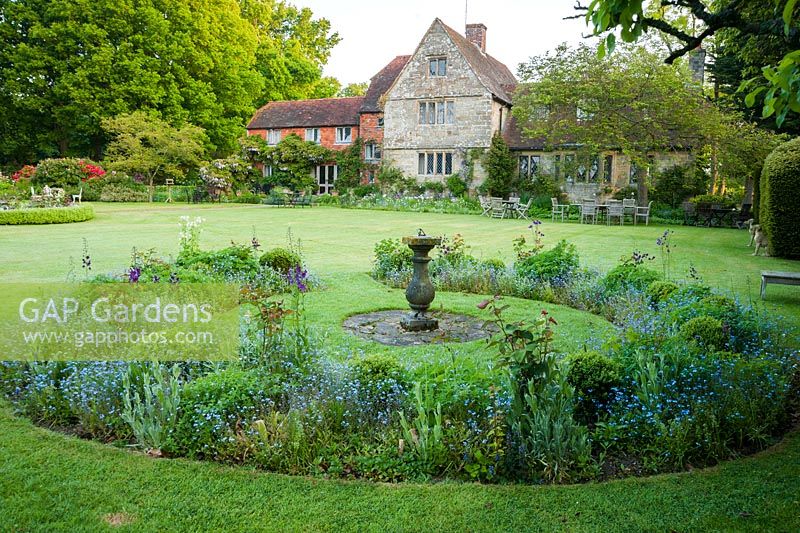 Formal garden in front of Grade II Jacobean manor house, with circular beds planted with verbascum, irises and forget-me-nots. King John's Nursery, Etchingham, East Sussex, UK