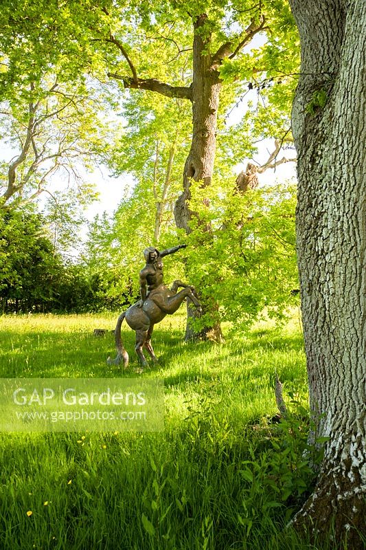 Fibreglass centaur sited amongst mature trees in the pasture around the garden. King John's Nursery, Etchingham, East Sussex, UK