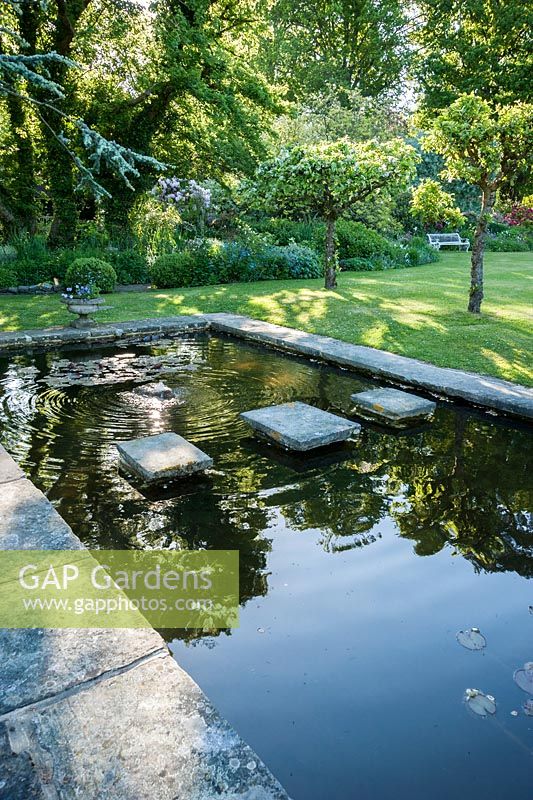 Formal pond with stepping stones that acts as a watery ha ha between the garden and surrounding fields. King John's Nursery, Etchingham, East Sussex, UK