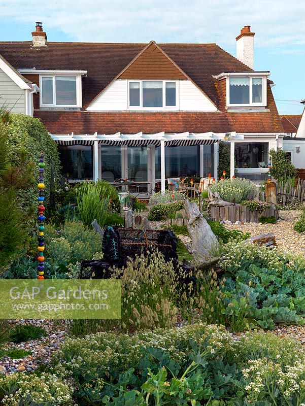 An exposed seaside garden is laid to shingle, with raised beds contained within driftwood, and planted with sea kale and quaking grass