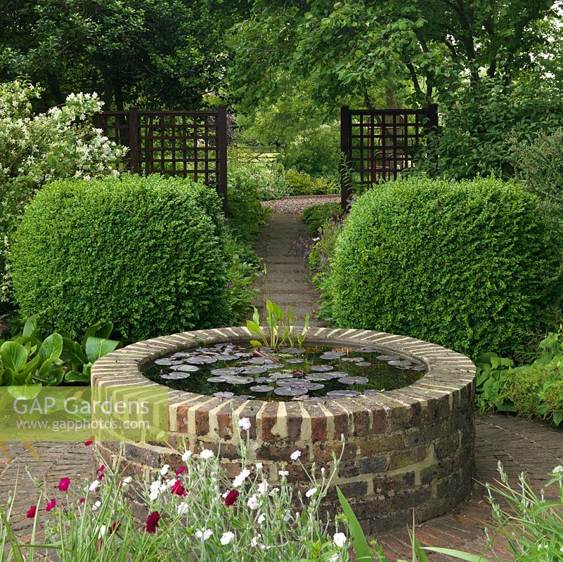A small raised pond provides a focal point at the end of a shady path.