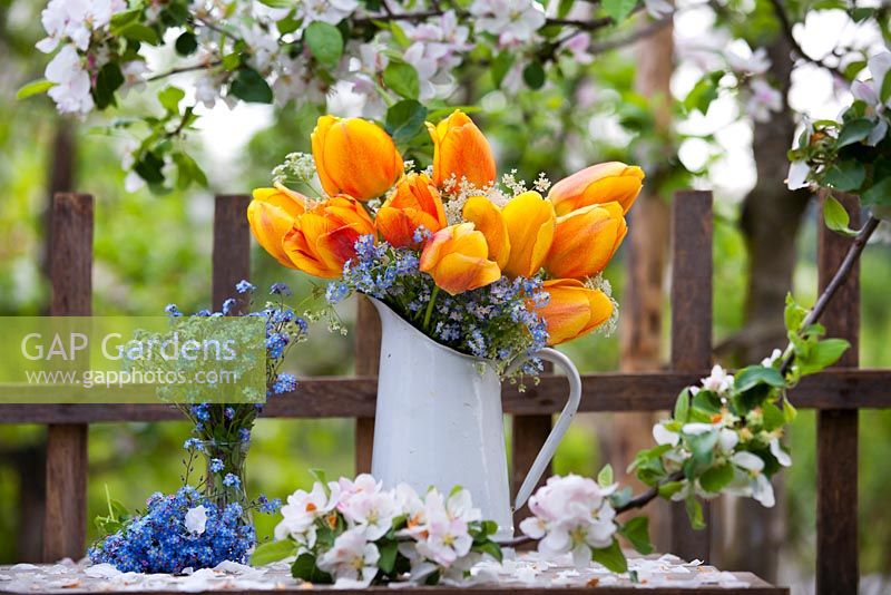 Floral arrangement with tulips, cow parsley and forget-me-nots on the table under a flowering apple tree.