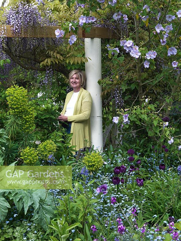 Vivien Cantor leans against a pergola pillar in her walled, quarter-acre London garden, by a spring bed of erysimum, forget-me-not, tulip, abutilon, euphorbia, camassia.