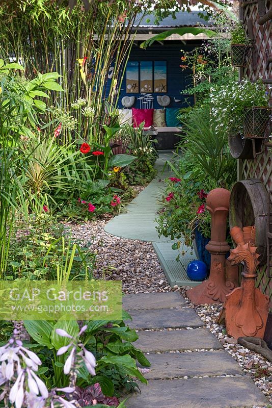 A small town garden with tropical foliage plants including bamboo with path leading to a secluded seating area.