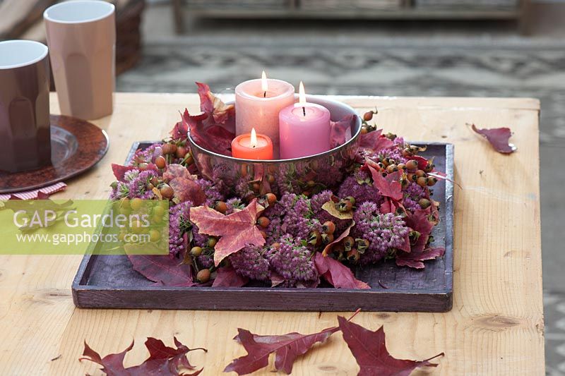 Wreath of Sedum - stonecrop and Rosa - rose hips on wooden coasters, silver bowl with candles in the middle, red autumn leaves