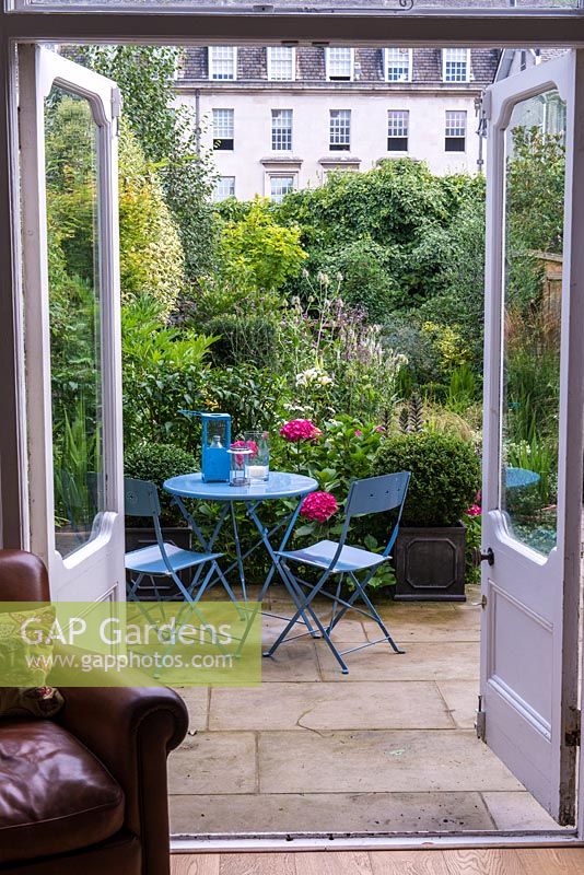 View from the house to a patio seating area in a densely planted town garden.