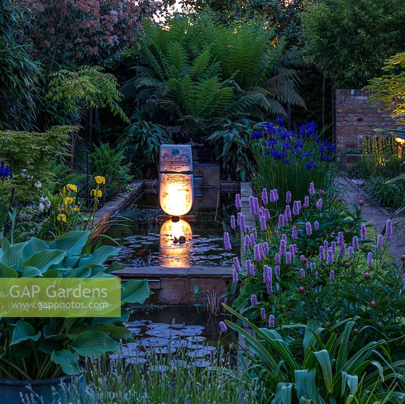 Lit at night,  long pool edged in hostas, lavender, Hakonechloa macra, Persicaria bistorta Superba, Iris sibirica 'Caesar's Brother' and male ferns. Pond sculpture by Peter Hayes.