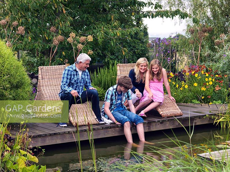 Joanne and Graham Winn with their children Sebastian and Scarlet relaxing on the pond side deck. Surrounding plants include Verbena, Helenium and Angelica gigas.