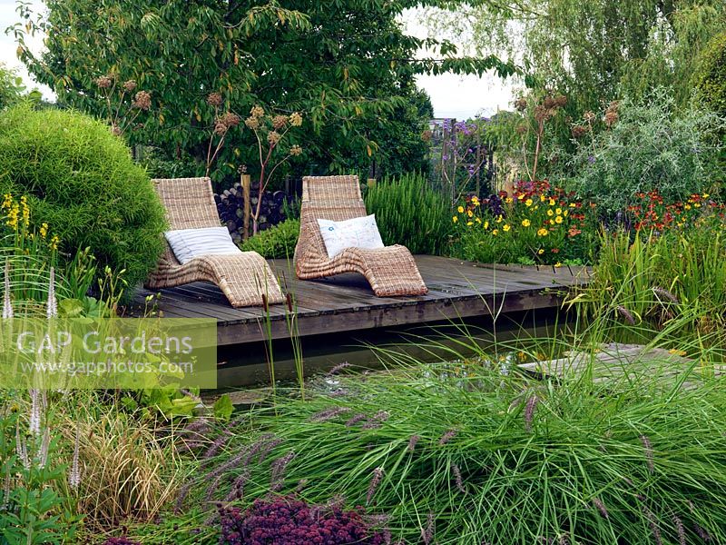 Wicker loungers on the pond side deck surrounded by Coreopsis, Helenium and Angelica gigas. Veronicastrum virginicum 'Fascination', Sedum telephium 'Purple Emperor' and Pennisetum alopecuroides are planted in the foreground.