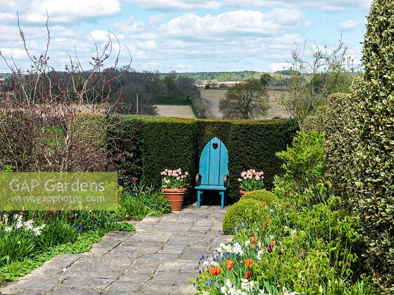 An ornamental seat draws the eye down a path lined with Tulipa Ballerina, Narcissus Thalia and Muscari armeniacum, to the Sussex countryside beyond.